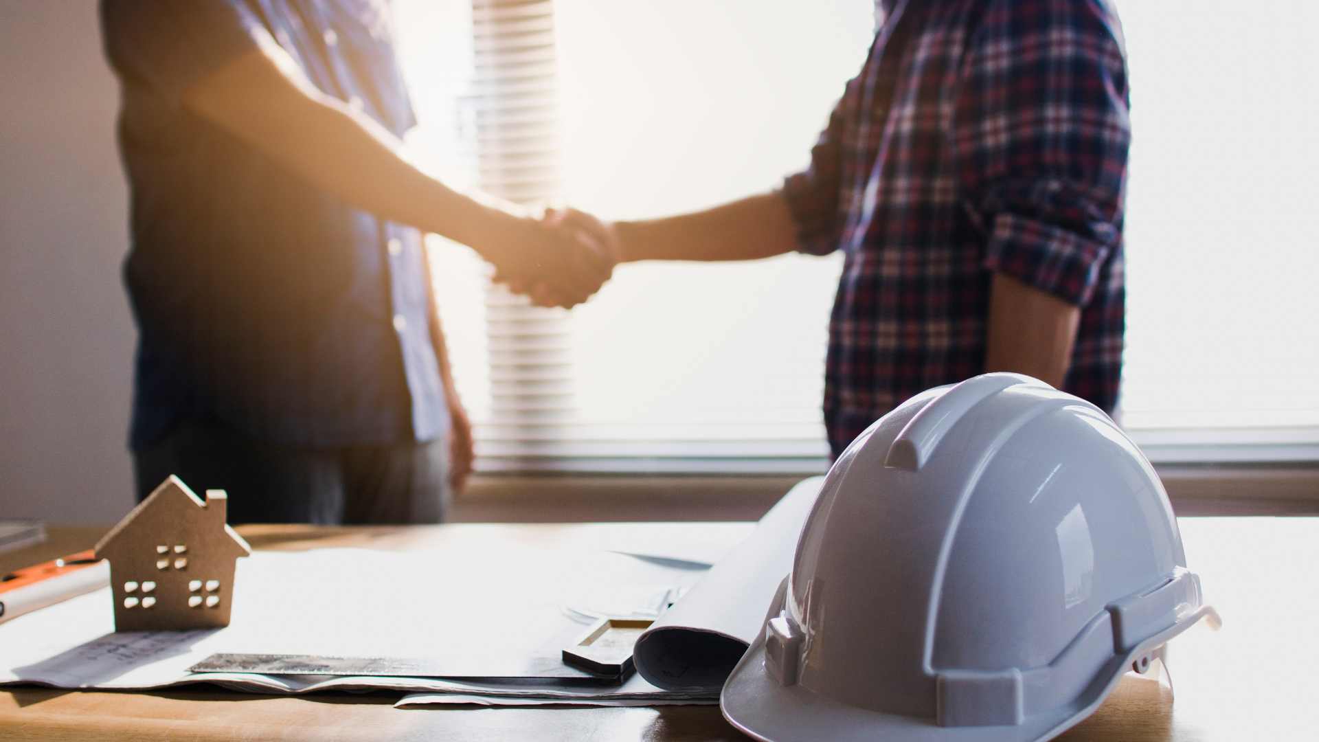 Handshake over building plans with hard hat